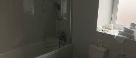 A bathroom with a bathtub, toilet, and a window with towels.