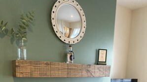 A room with a black wood-burning stove, a mirror above it, and a shelf with a plant and a framed certificate. - Pier 36 (Donaghadee)