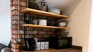 A compact kitchen with a brick accent wall, a coffee maker, a microwave, and a shelf with plates and cups. - Pier 36 (Donaghadee)