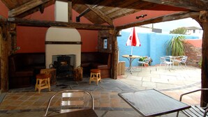 An outdoor patio with stone flooring, wooden furniture, and a brick fireplace. - Pier 36 (Donaghadee)