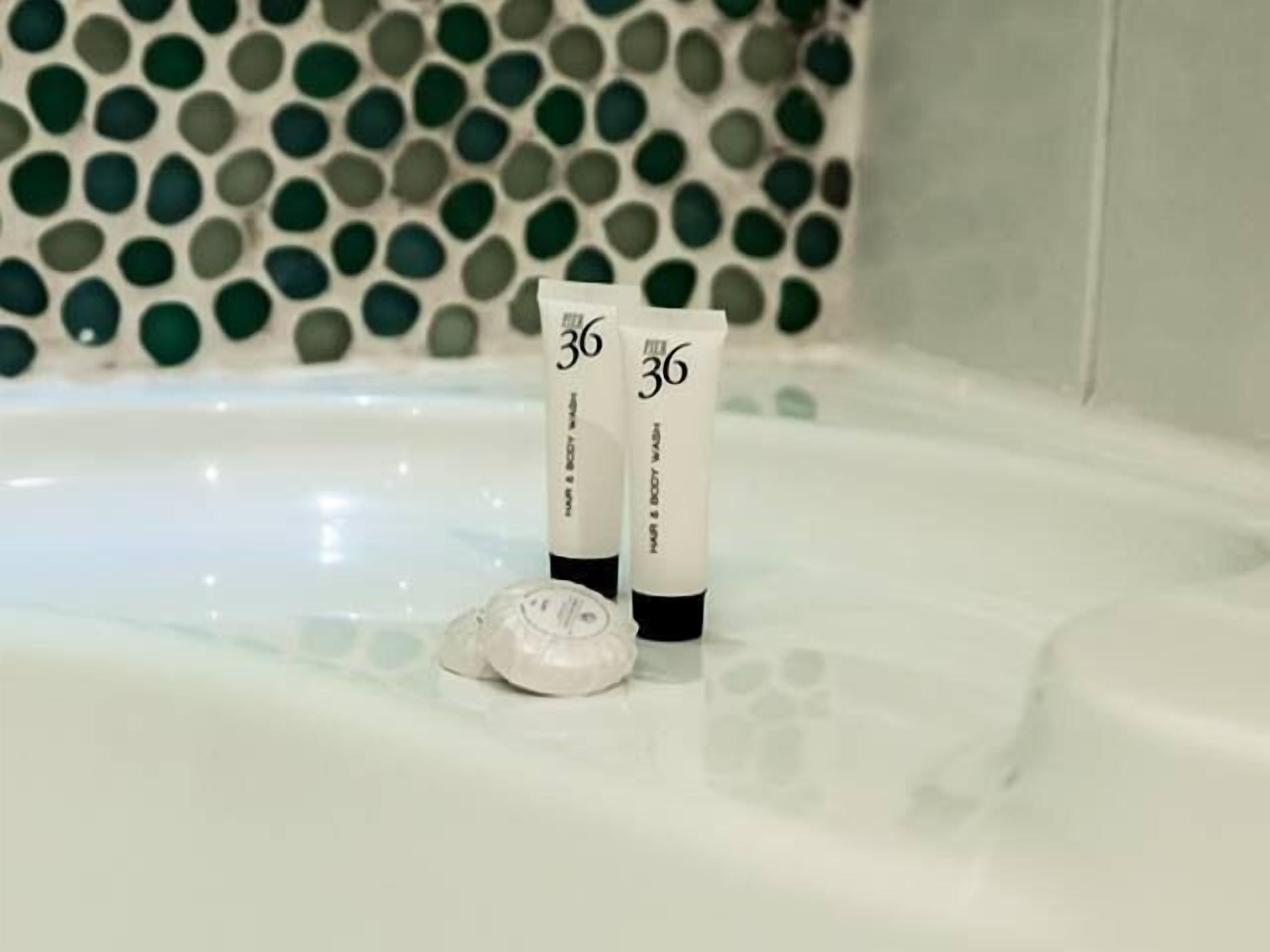 Dos botellas de gel de ducha en una bañera con un muro de azulejos decorativos al fondo.
