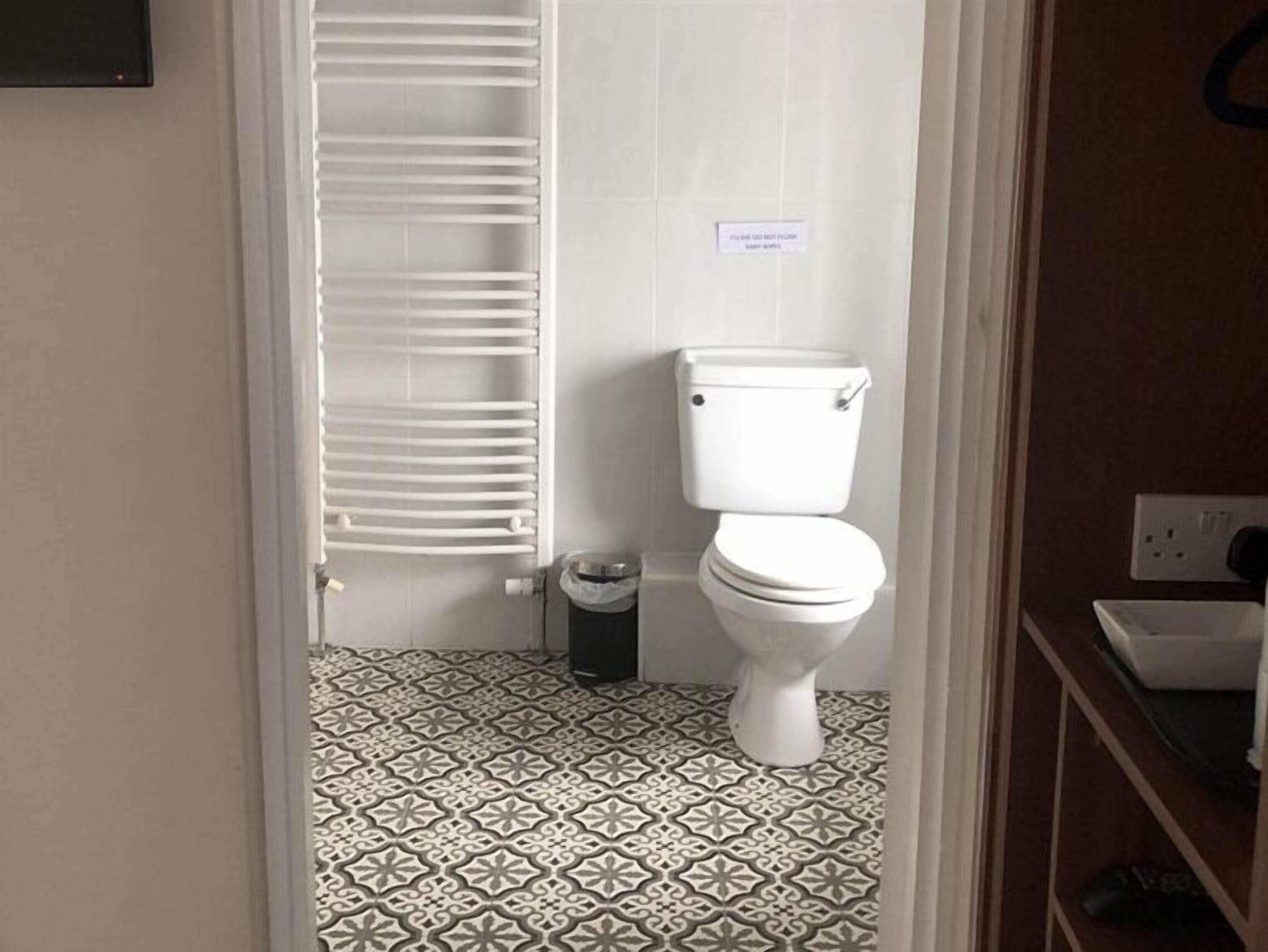 A bathroom with a toilet, a trash bin, and a towel rack.
