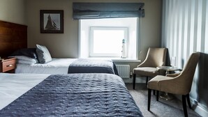A hotel room with two beds, a chair, a small table, a window with a view, and a radiator. - Pier 36 (Donaghadee)