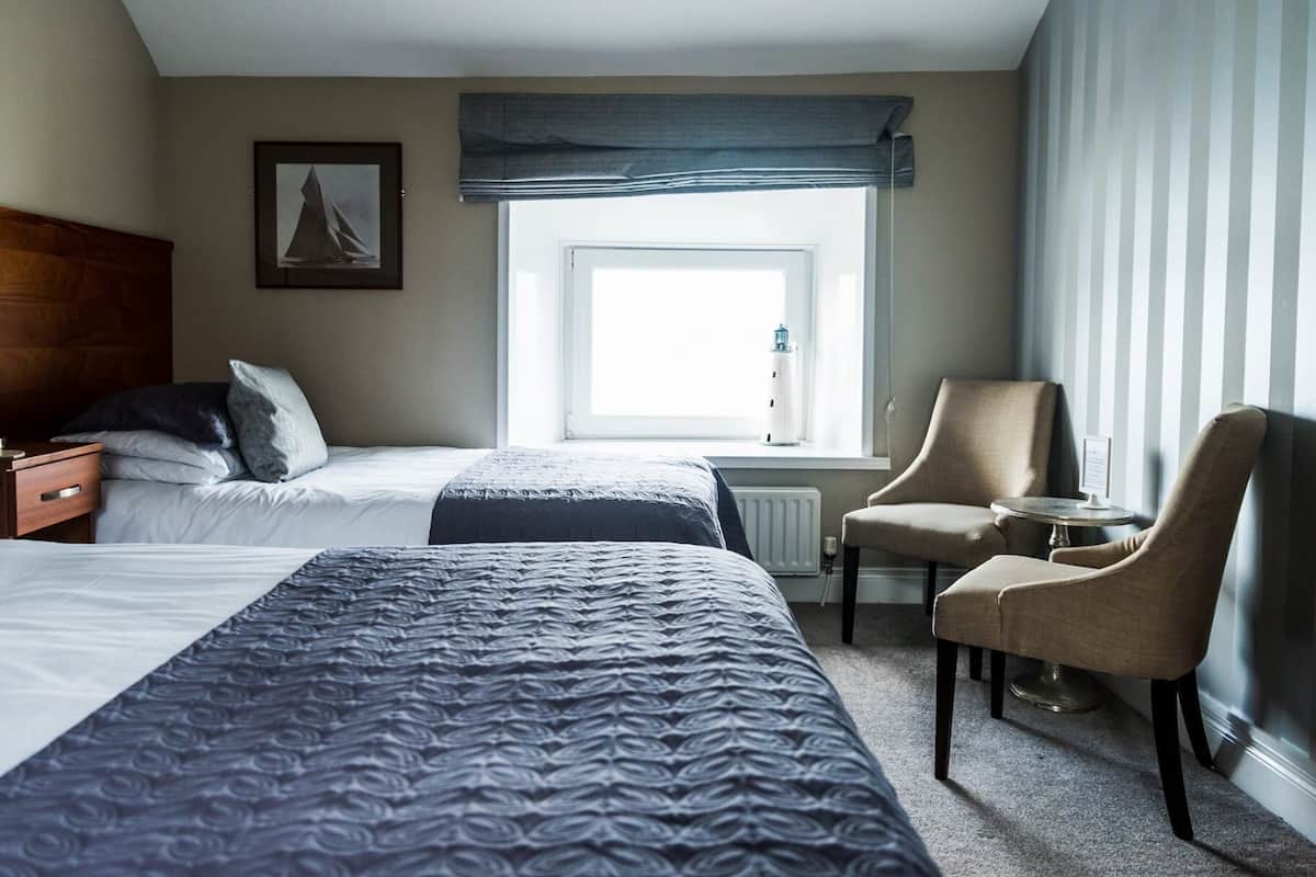 Ein Hotelzimmer mit zwei Betten, einem Sessel, einem kleinen Tisch, einem Fenster mit Blick und einer Heizung.