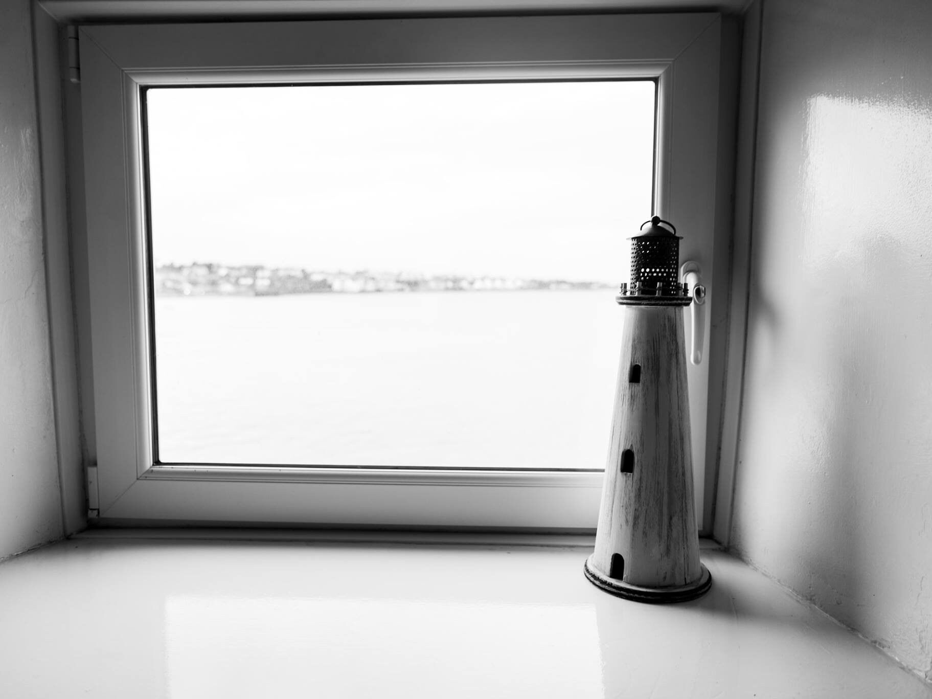 Una ventana con vistas al agua y un faro en el alféizar.