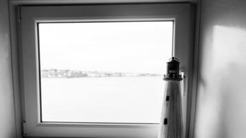 Una ventana con vistas al agua y un faro en el alféizar.