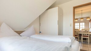 A bedroom with two beds, a desk, and a chair in the corner. - Apartment upper floor center (ID 184) (Sankt Peter-Ording)