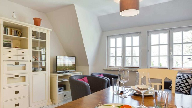 A dining area with a wooden table set for two, a television, and a white cabinet with drawers. - Apartment upper floor center (ID 184) (Sankt Peter-Ording)
