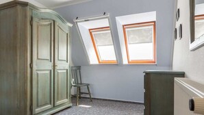 A room with a large wardrobe, a radiator, and two windows with skylights. - Apartment upper floor center (ID 184) (Sankt Peter-Ording)