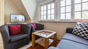 A cozy living room with a television, two sofas, a coffee table, and large windows. - Apartment upper floor center (ID 184) (Sankt Peter-Ording)