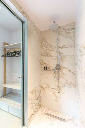Une salle de bain moderne dotée d’une douche à parois de verre, de murs en marbre et d’une étagère intégrée pour les articles de toilette.