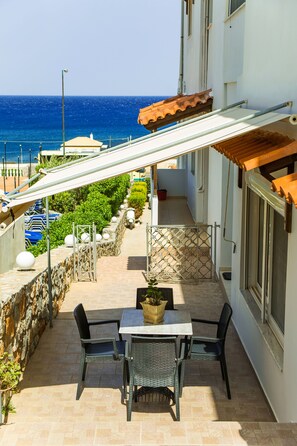 Un balcon avec une table et des chaises, une plante en pot et une vue sur la mer.