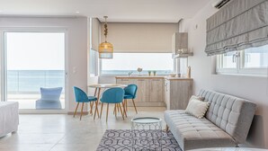 Una sala de estar moderna con un sofá, una mesa de comedor con sillas, una zona de cocina y un ventanal con vista al mar.