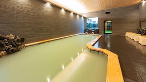 Ein moderner Innenpool mit Holzbalkendecke und -wänden, mit freiem Blick ins Freie und einer Sitzecke mit Hockstühlen.
