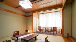 Ein traditioneller japanischer Raum mit Tatami-Böden, einem niedrigen Tisch mit kariertem Tischtuch, einer gepolsterten Sitzbank und einem Futon-Bett.