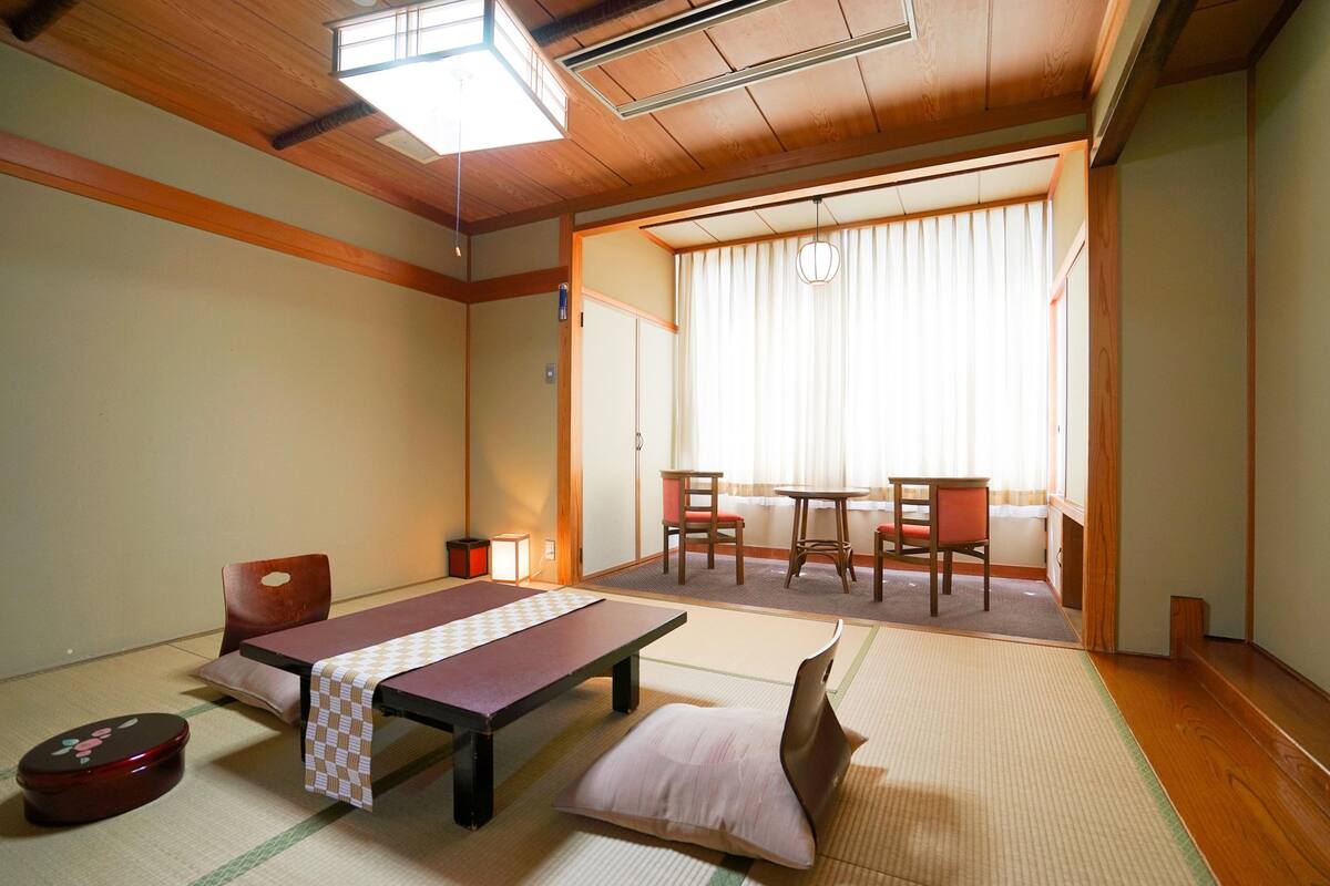 Une pièce de style japonais traditionnel, avec un sol recouvert de tatamis, une petite table recouverte d’une nappe à carreaux, un banc rembourré et un futon servant de lit.
