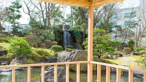 Eine Holzterrasse mit Blick auf einen Garten, der einen Wasserfall, Felsen und verschiedene Pflanzen zeigt.