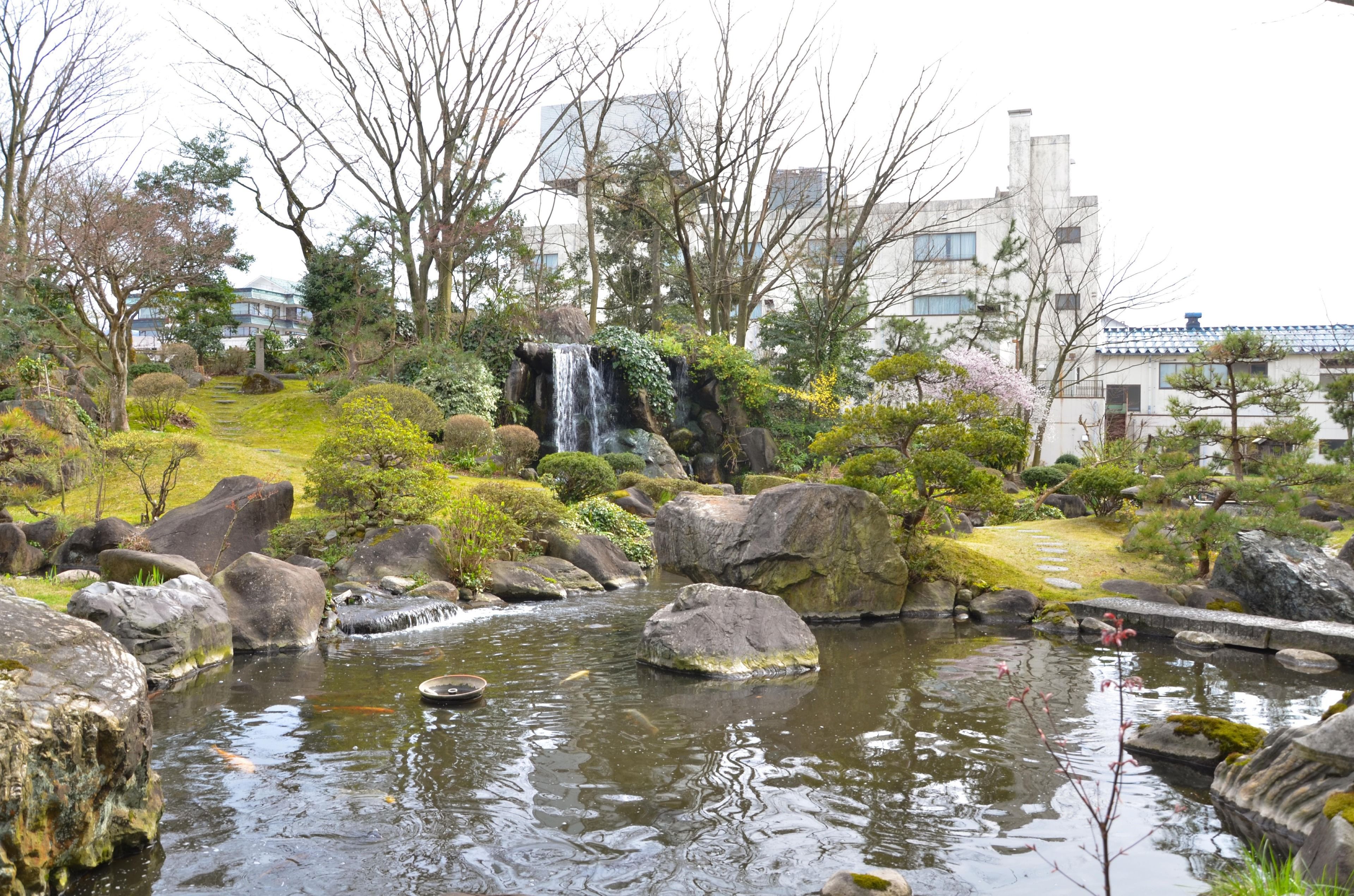 A serene garden with a small waterfall, large rocks, and a pond.
