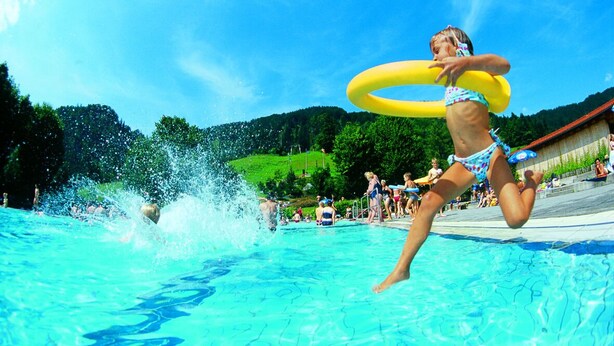A swimming pool with clear blue water, surrounded by a grassy area and trees.