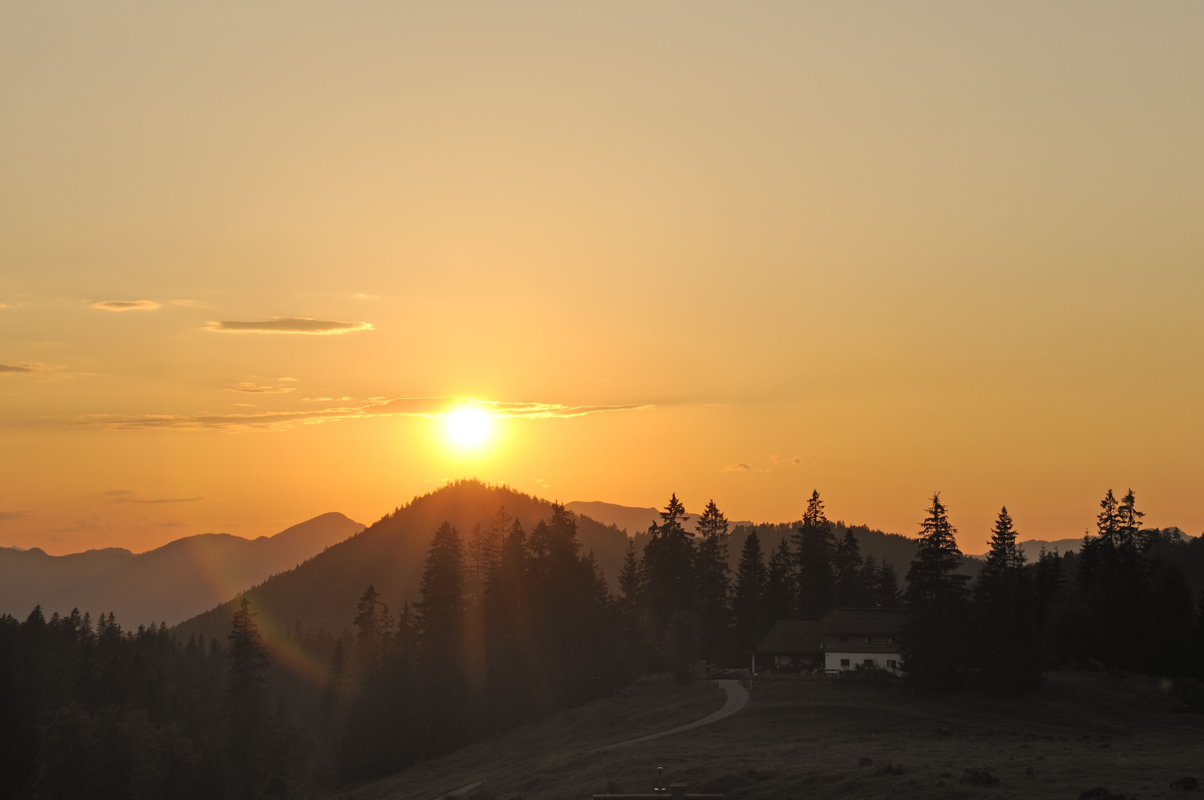 A sunset over a mountainous landscape with a path leading to a building.