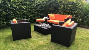 A patio area with a black wicker sofa set, a matching coffee table, and a small decorative table with a vase and candle.