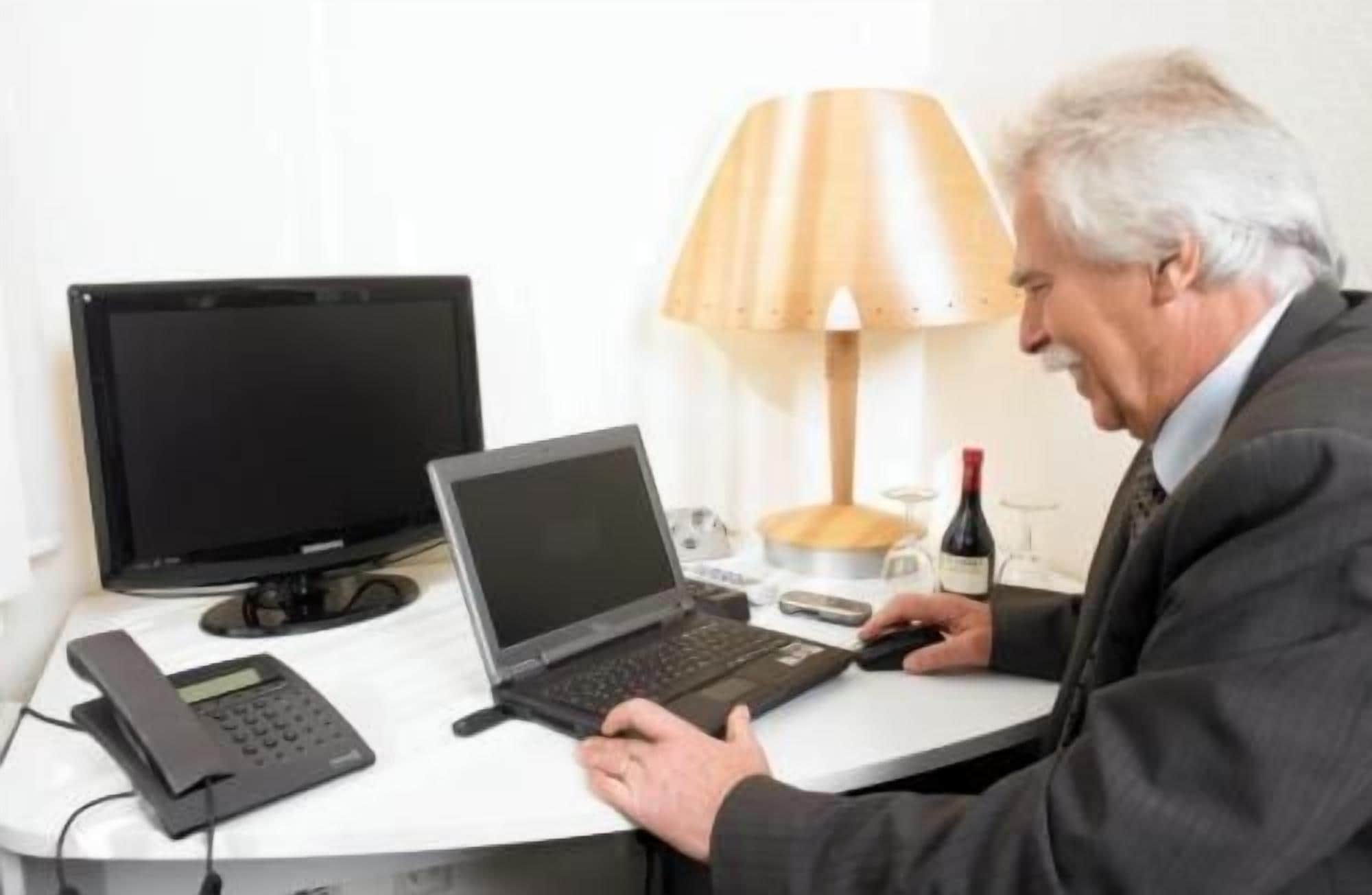 A person using a laptop at a desk with a telephone, a lamp, and a wine bottle.