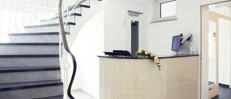 Un área de recepción moderna con una escalera curva, un mostrador de recepción y una pantalla montada en la pared.
