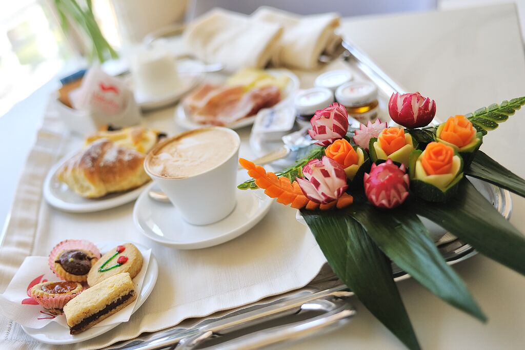 Ein Frühstücksbrett mit Gebäck, einer Kaffeetasse und einer Blumenkomposition.