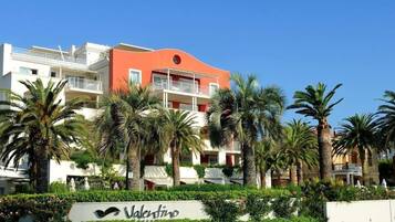 Un hotel de varios pisos con balcones, palmeras y un letrero que dice 'Valentino'.
