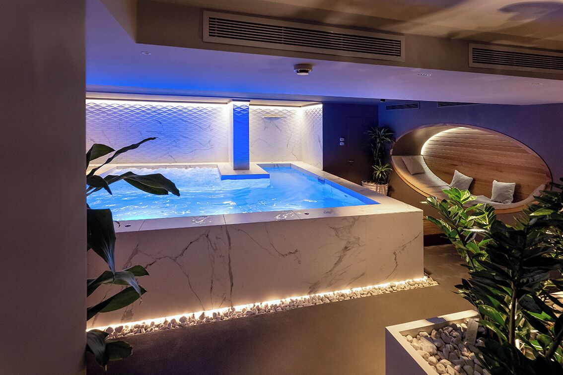 A spa area with a hot tub, marble walls, and a wooden seating area.