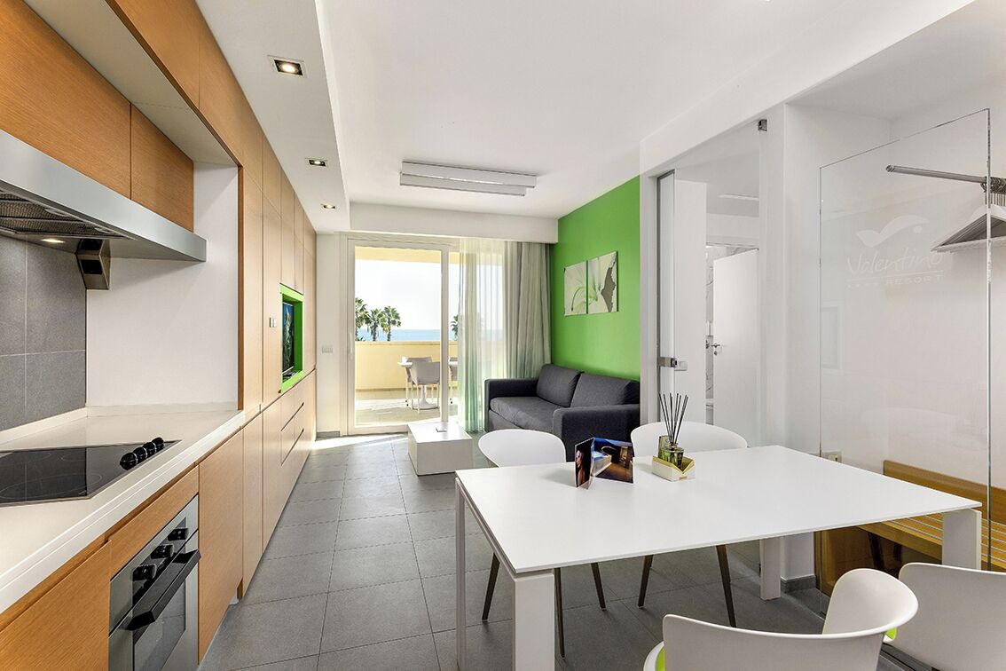 A modern kitchen with a built-in stove, a dining area with a white table and chairs, and a green accent wall.