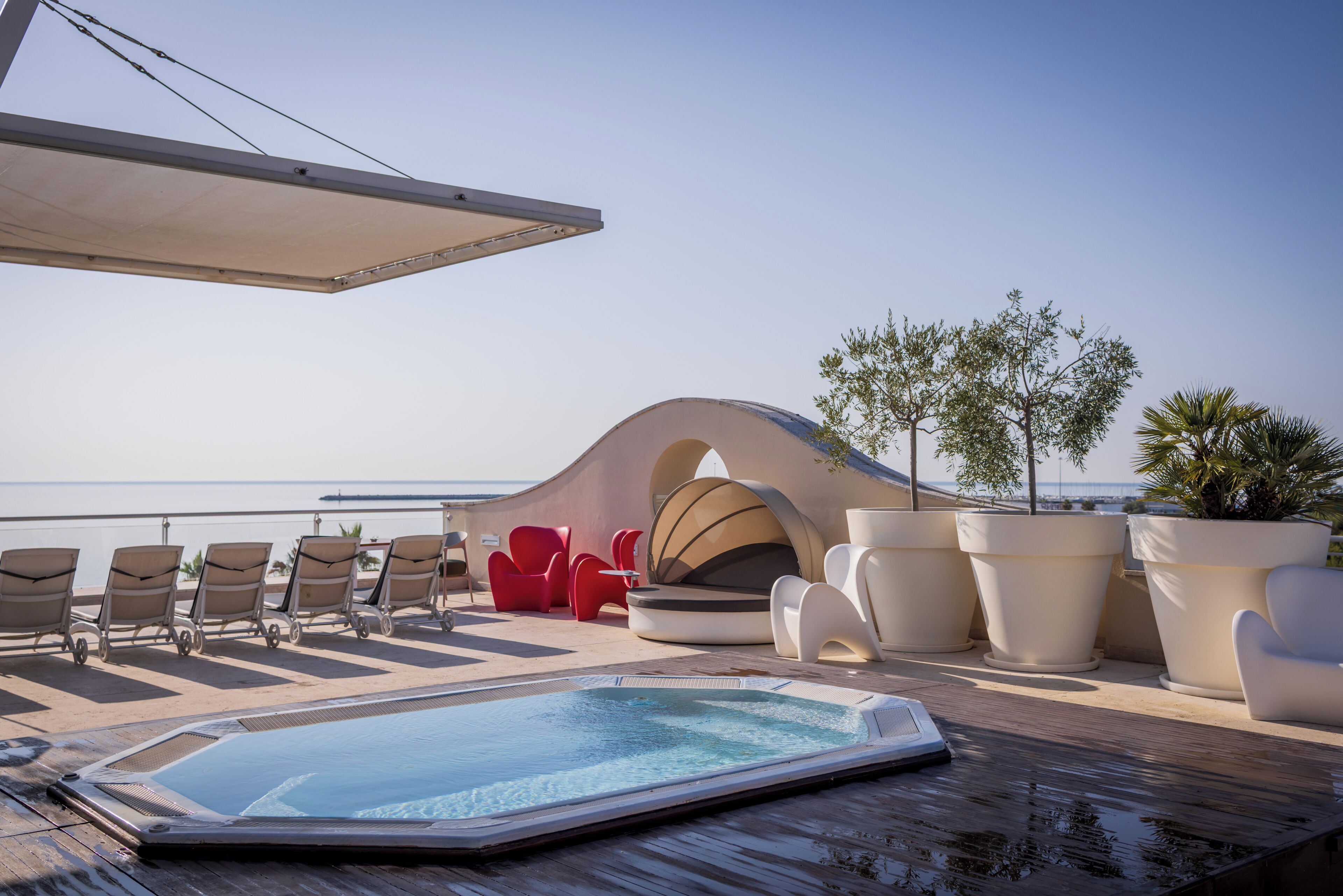 A rooftop pool area with lounge chairs, a hot tub, and potted plants.