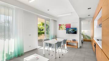 Una cocina moderna con armarios blancos, un área de comedor con mesa y sillas blancas, y un televisor montado en la pared.