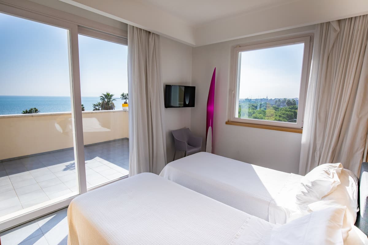 Habitación de hotel con dos camas, televisión y balcón con vista al mar.