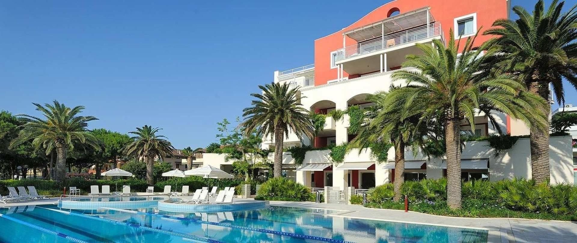 A resort with multiple swimming pools, palm trees, and a building with balconies.