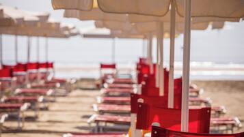 Beach chairs and umbrellas arranged in rows on a sandy beach.