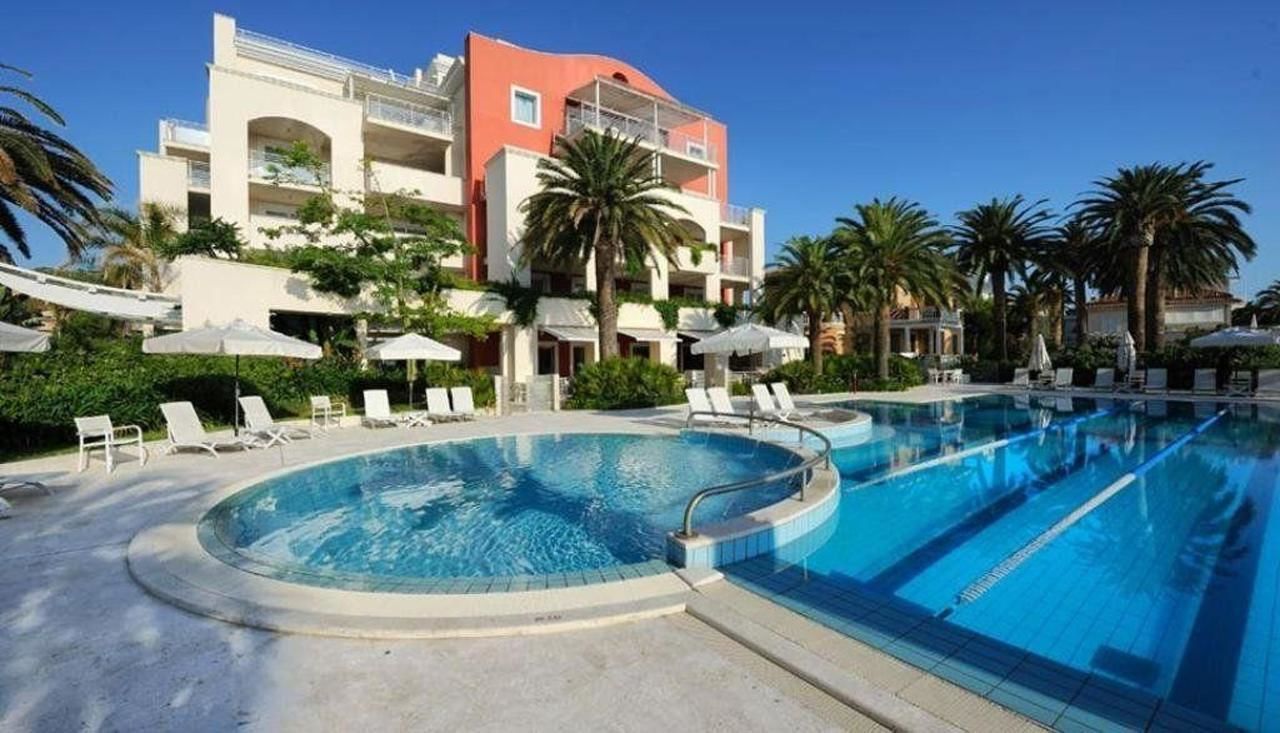 Un hotel con una piscina grande, tumbonas y palmeras.