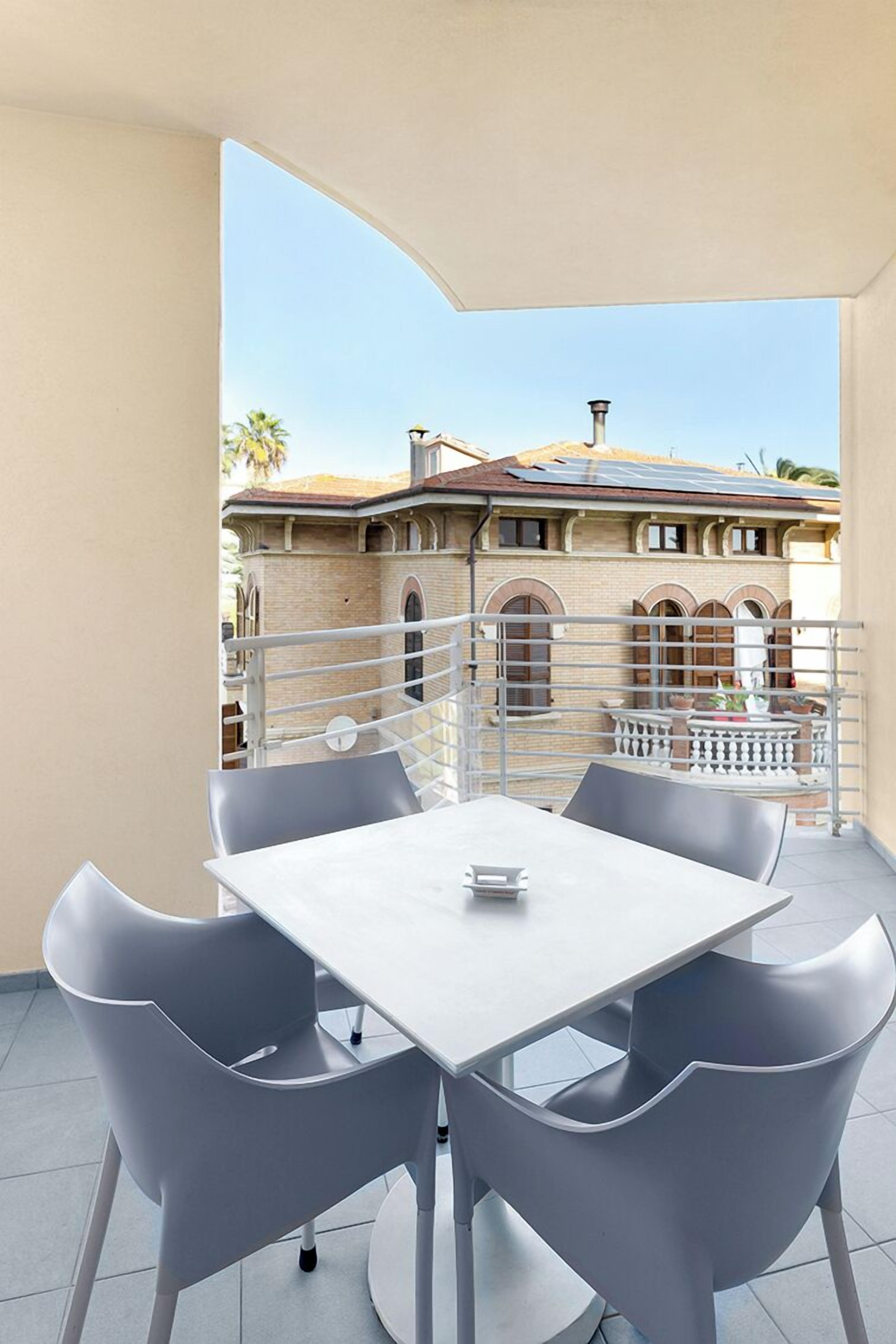 A balcony with a table and chairs, a view of a building with arched windows, and a railing.
