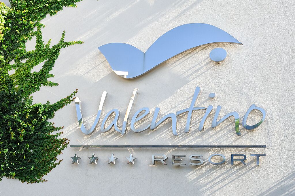 A sign for Valentino Resort with a stylized 'V' and the word 'Valentino' in a cursive font, along with the word 'RESORT' in capital letters.