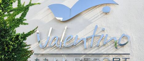 A sign for Valentino Resort with a stylized 'V' and the word 'Valentino' in a cursive font, along with the word 'RESORT' in capital letters.