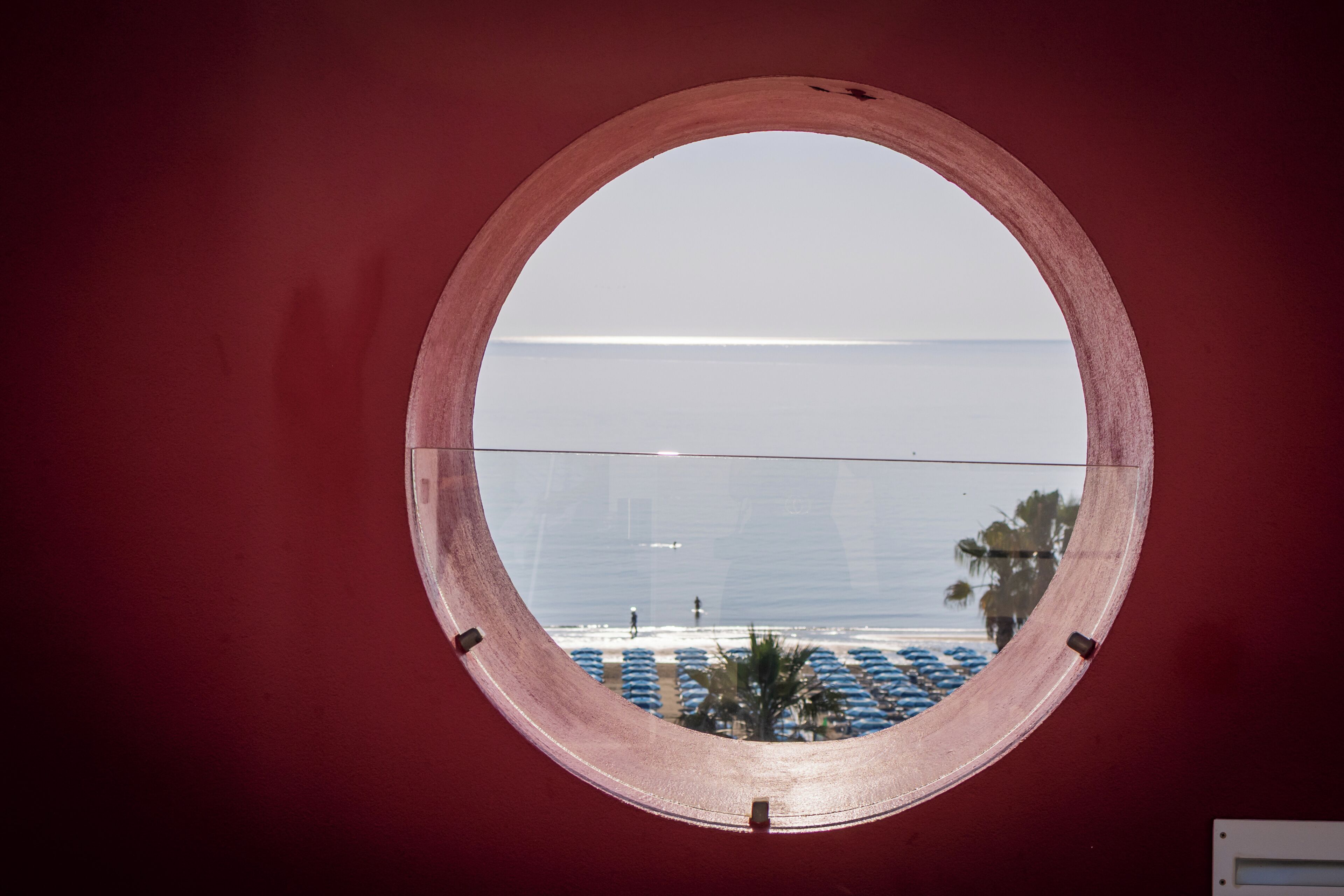 A circular window with a view of a beach and umbrellas.