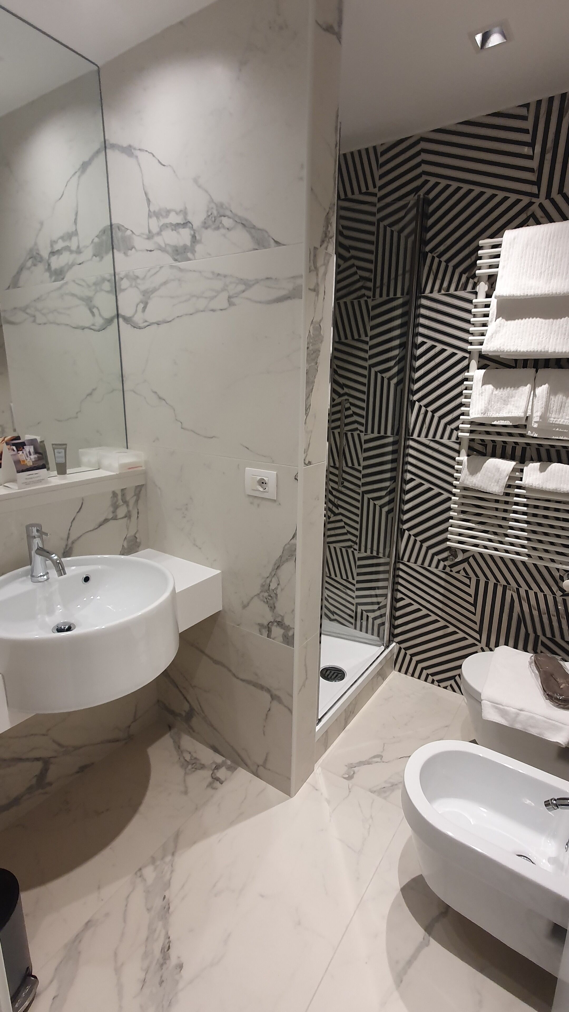 A bathroom with a marble sink, a mirror, a toilet with striped wallpaper, and a bathtub.