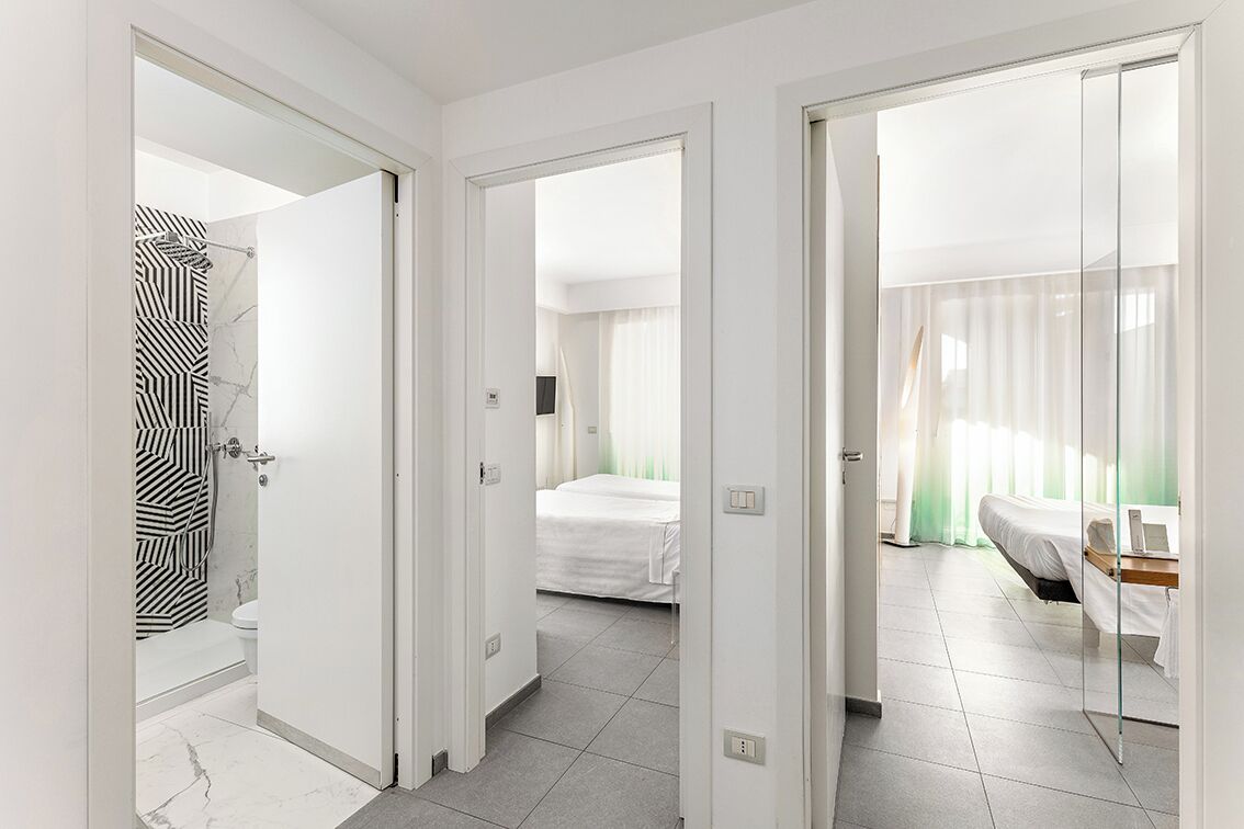 A hotel room with a bathroom, a bed, a desk, and a window with curtains.