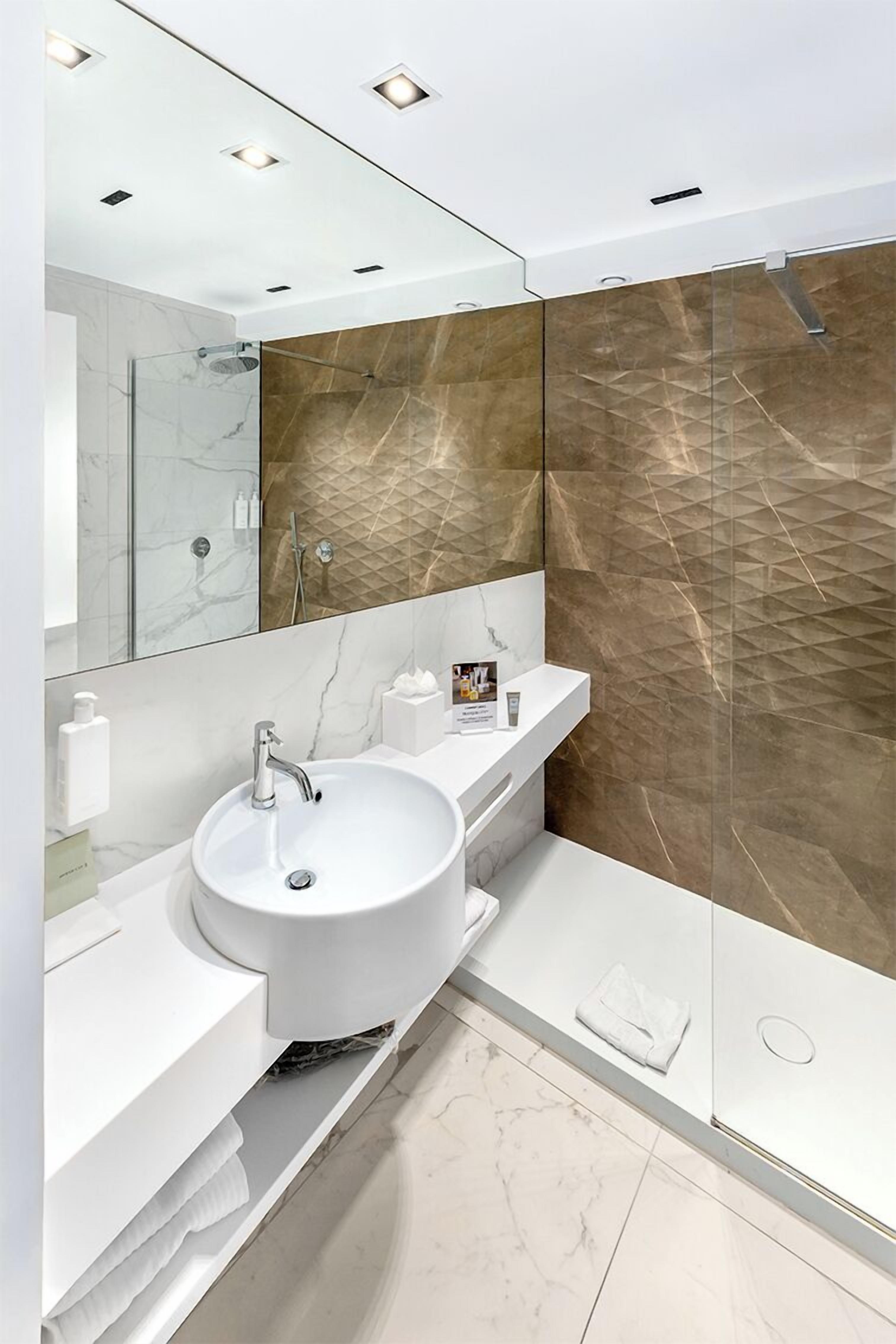 A modern bathroom with a white sink, marble countertop, and a glass shower enclosure.