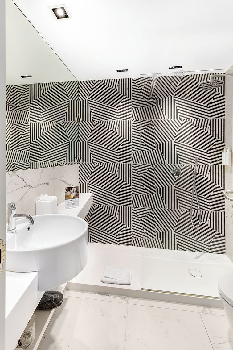 Un bagno moderno con parete a motivi geometrici, un lavandino rotondo e una zona doccia.