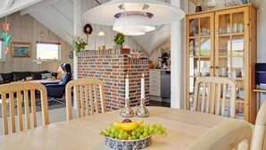 A dining area with a brick fireplace, wooden chairs, a table with a fruit bowl, and a glass cabinet with dishes. - Pet friendly home in Hvide Sande with WiFi (Hvide Sande)