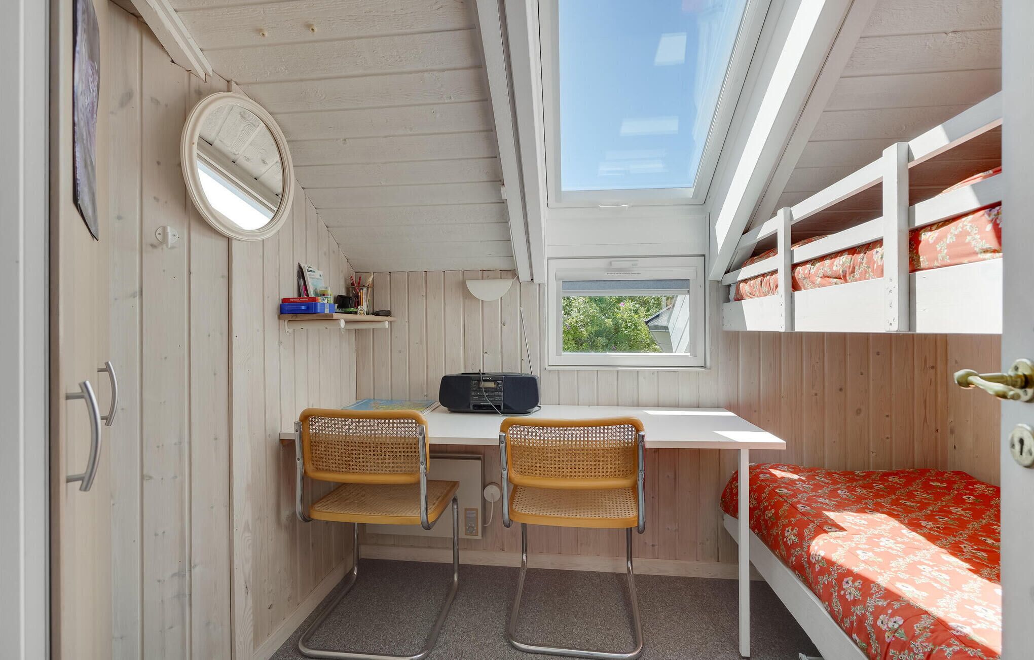 A compact room with a bunk bed, a desk with two chairs, a mirror, and a window.
