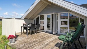 A covered patio with a table and chairs, a green cushioned chair, and a flower pot. - Pet friendly home in Hvide Sande with WiFi (Hvide Sande)