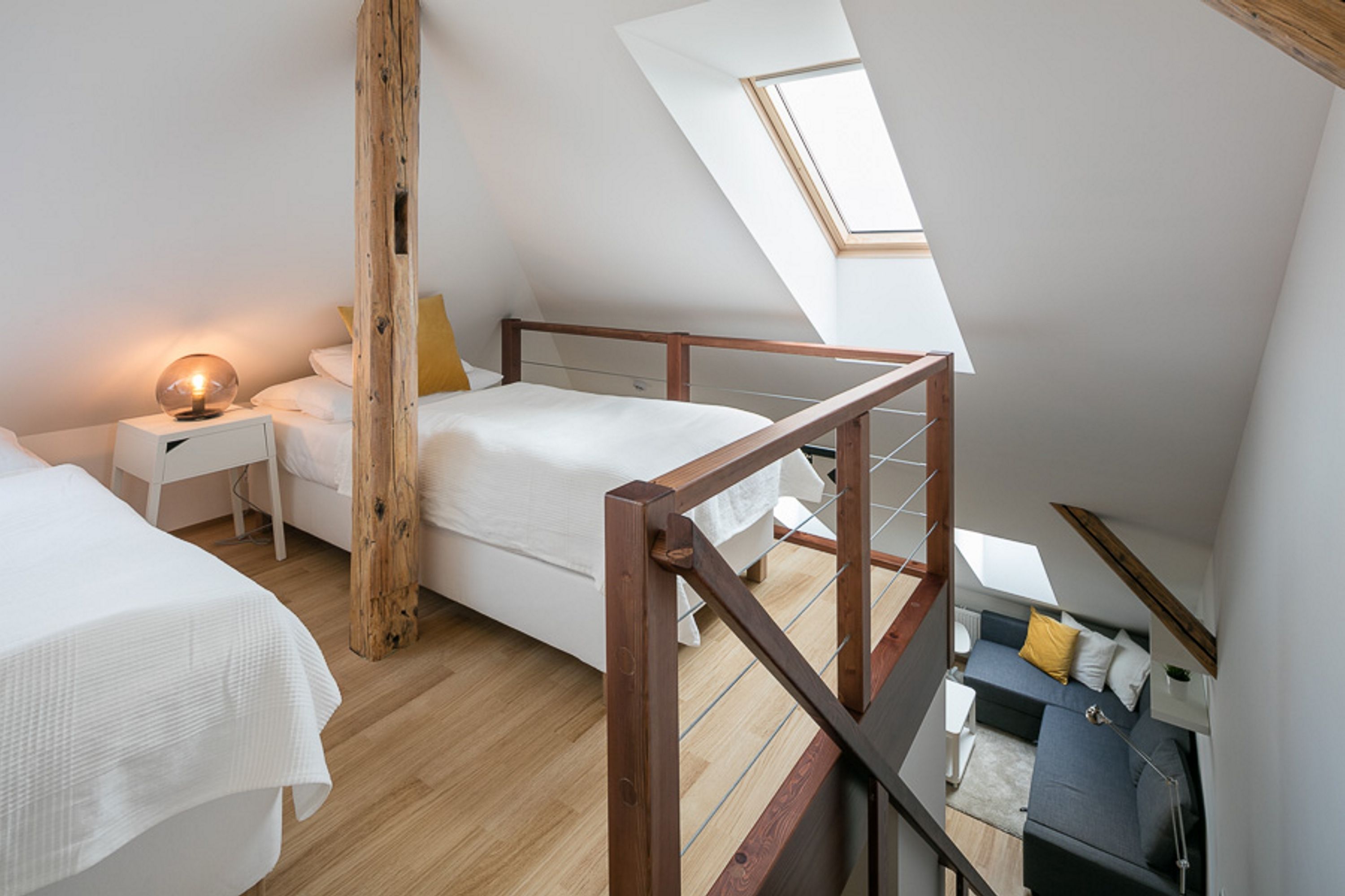 Une chambre de style loft moderne, avec un plafond en pente, des poutres en bois, une lucarne, un lit, un bureau et un canapé.