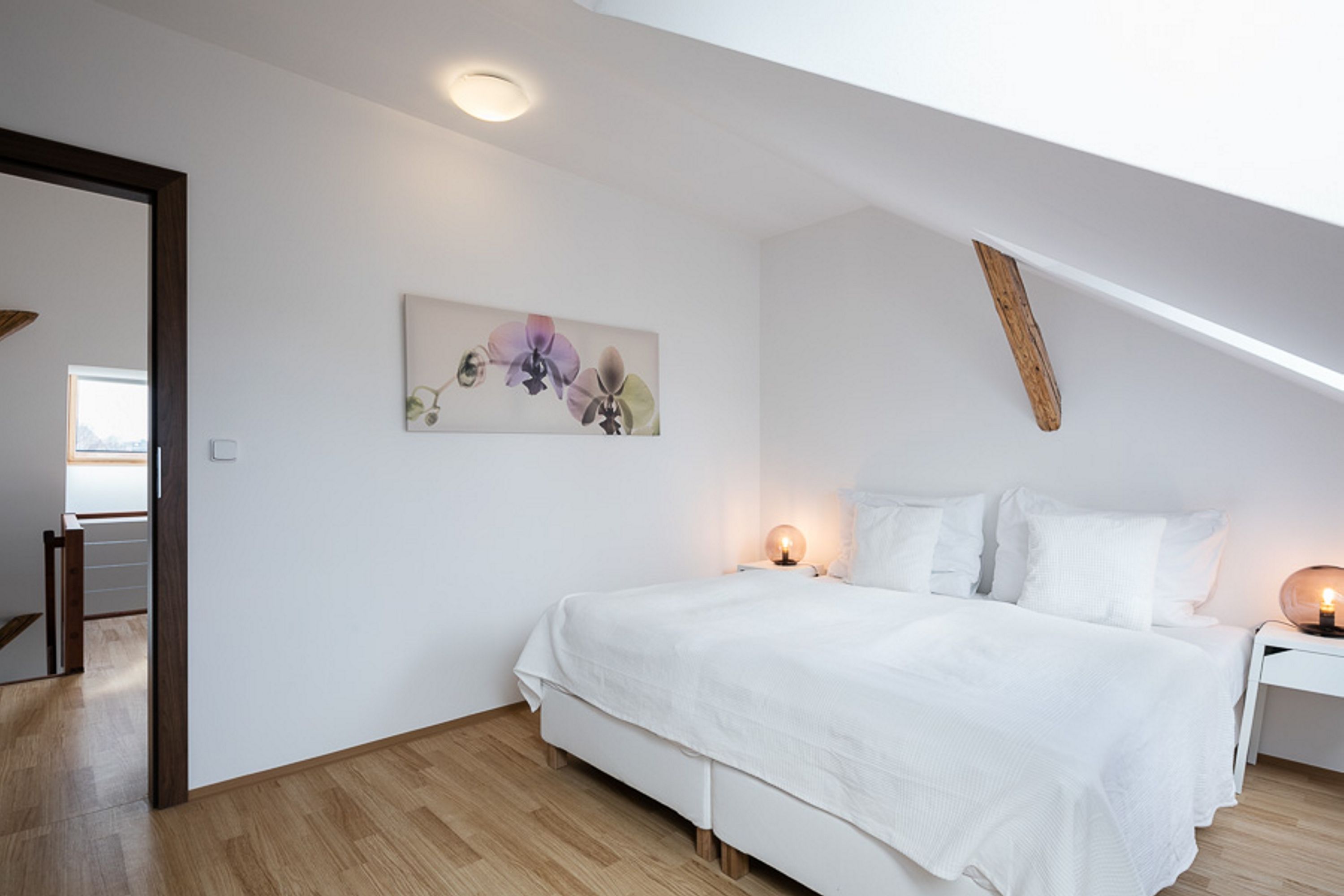 A bedroom with a large bed, a nightstand, a wall-mounted lamp, and a ceiling light.